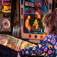 The back of a young girl playing pinball